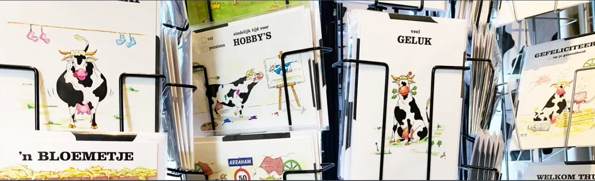 Assortiment wenskaarten met koeienillustraties in een kaartenrek