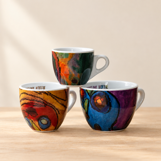 Drie Hesselink koffiekopjes met kleurige patronen op lichte houten ondergrond